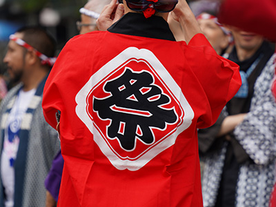 Un homme porte un haori, une veste rouge avec un kanji dans le dos.